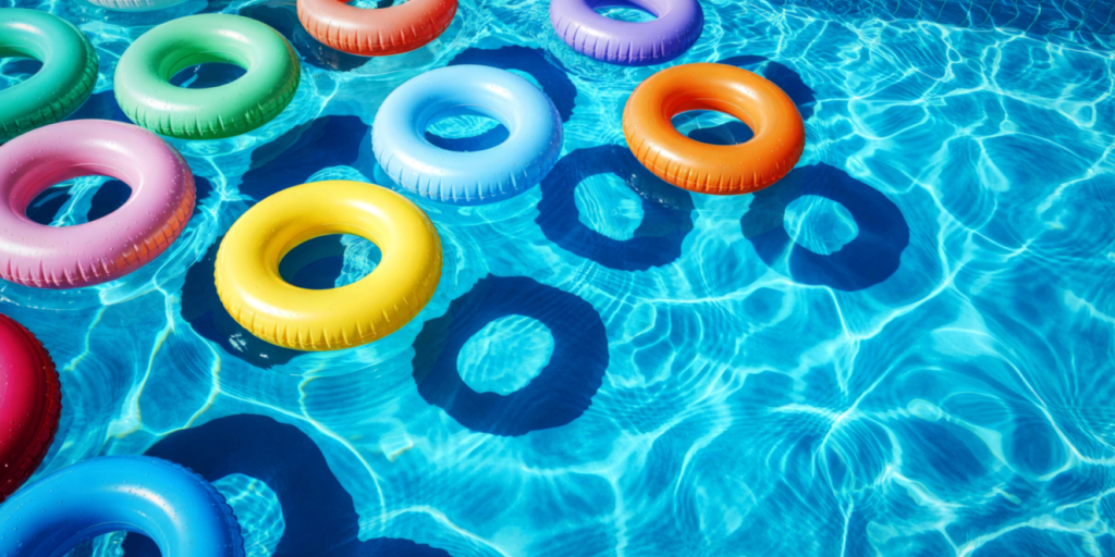 Colorful inflatable rings floating on bright blue pool water, casting circular shadows in a sunny, playful scene.