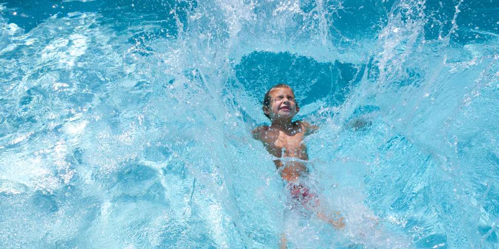 Child splashing into a swimming pool, surrounded by water spray and waves.