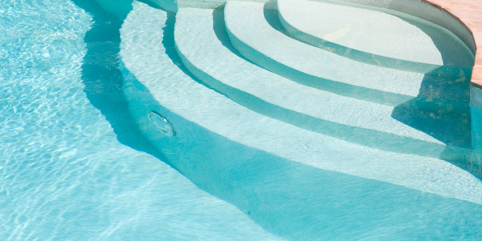 Close up view of shallow pool entry steps with sunlight reflecting through clear turquoise water.