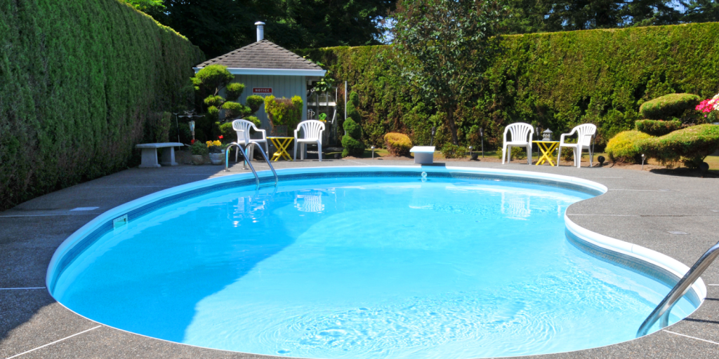 Backyard residential swimming pool surrounded by hedges, patio seating, and landscaped garden.
