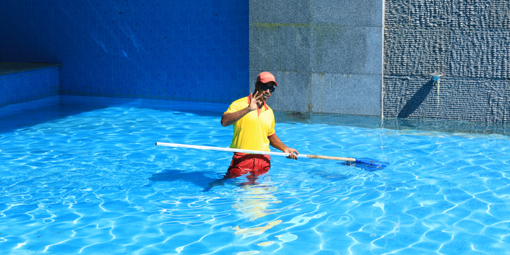 Pool maintenance professional cleaning a commercial swimming pool using a skimmer as part of routine pool management services.
