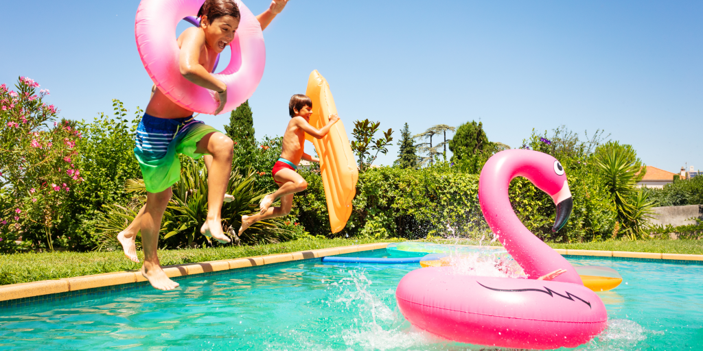 Children jumping into a swimming pool under supervised conditions, highlighting the importance of pool safety standards at recreational facilities.