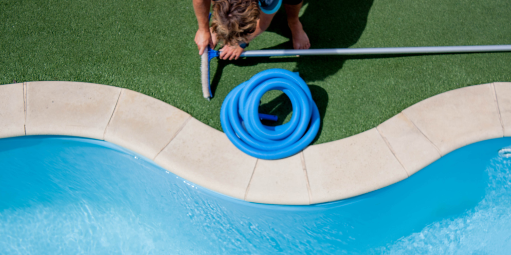 Overhead view of a person cleaning a swimming pool with a brush and blue hose.