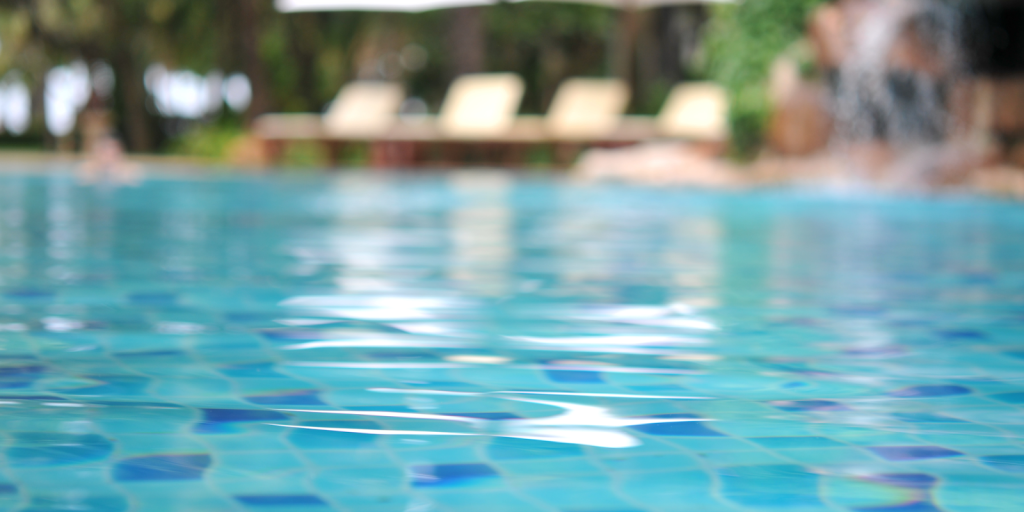 Close-up of calm swimming pool water with blurred lounge chairs in the background.