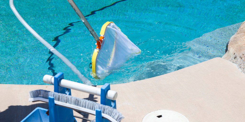Pool cleaning net skimming debris from clear blue water near the pool edge.
